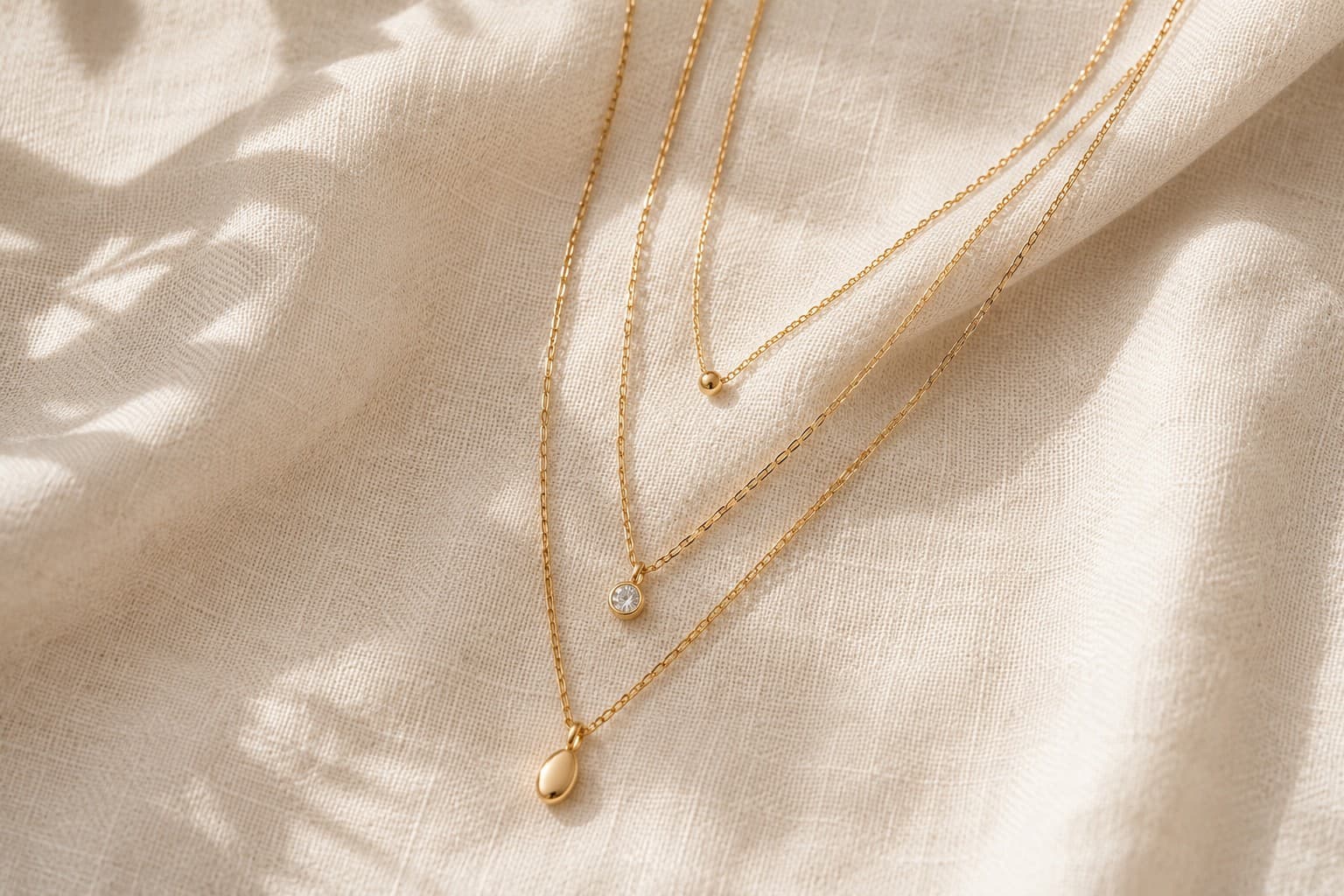 Layered thin gold chain necklaces on linen